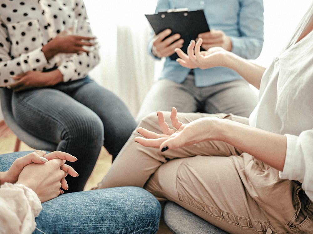 Close-up of a group therapy session, showing people sitting in a circle facilitated by a psychiatric mental health nurse practitioner