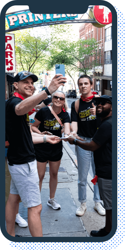 A phone containing a group of people on a city street in matching T-shirts taking a selfie of themselves.